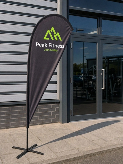Black teardrop flag for Peak Fitness standing outside the glass entrance doors of a gym